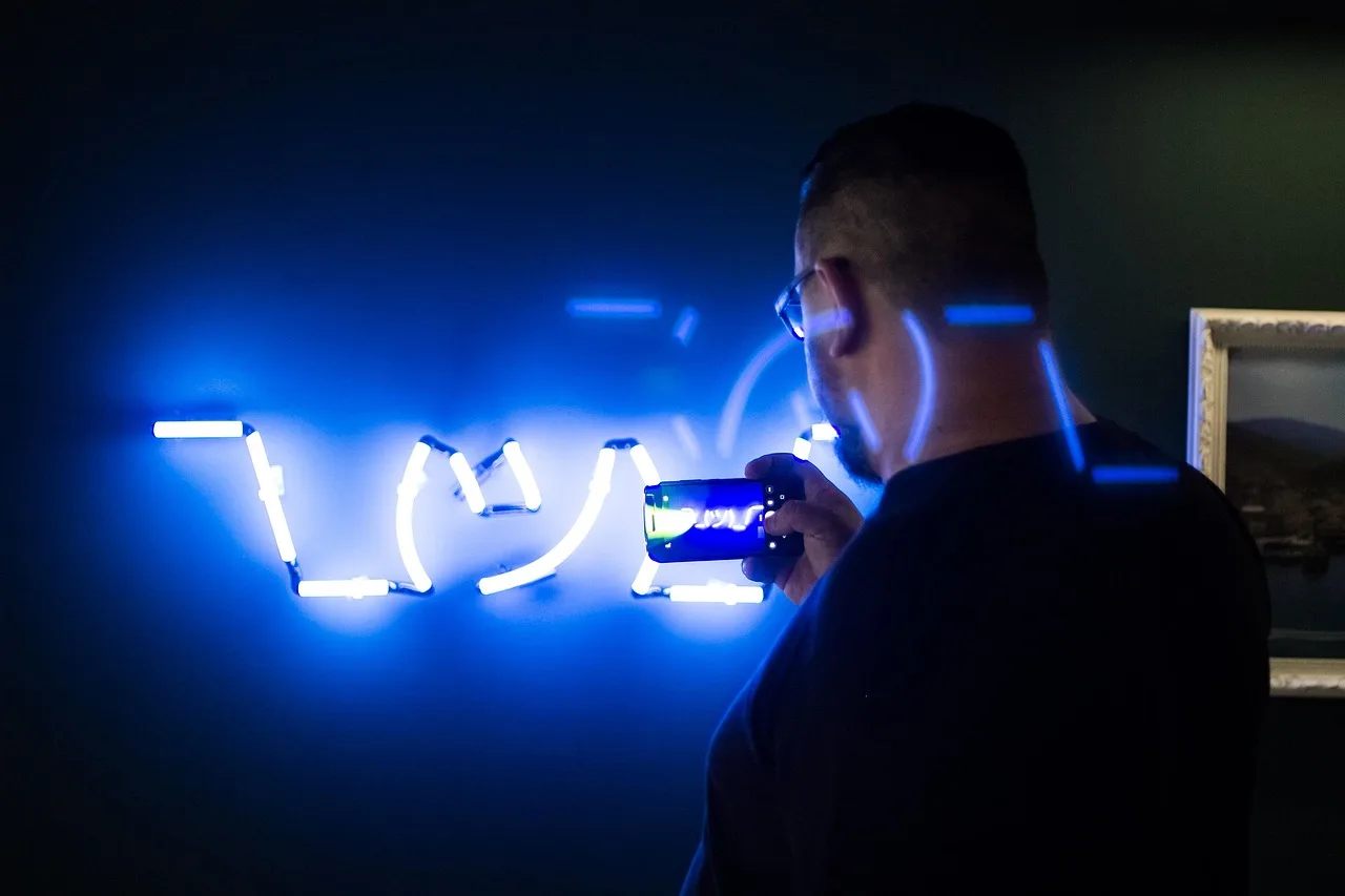 neon sign, man, mobile phone, phone camera, smartphone, taking picture, person, neon, neon blue, lights, glow, illuminated, signage, dark. Shooting neon sign restoration twice: flat daylight, then dusk