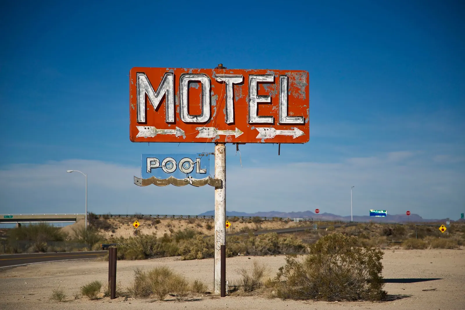 A vintage motel sign stands prominently in a desert landscape under a clear blue sky, evoking travel nostalgia.