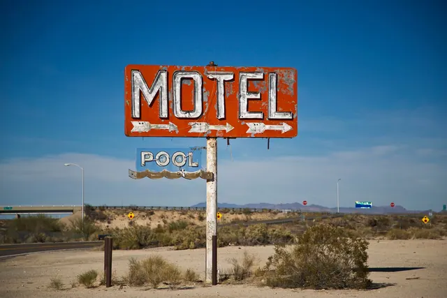 A vintage motel sign stands prominently in a desert landscape under a clear blue sky, evoking travel nostalgia.