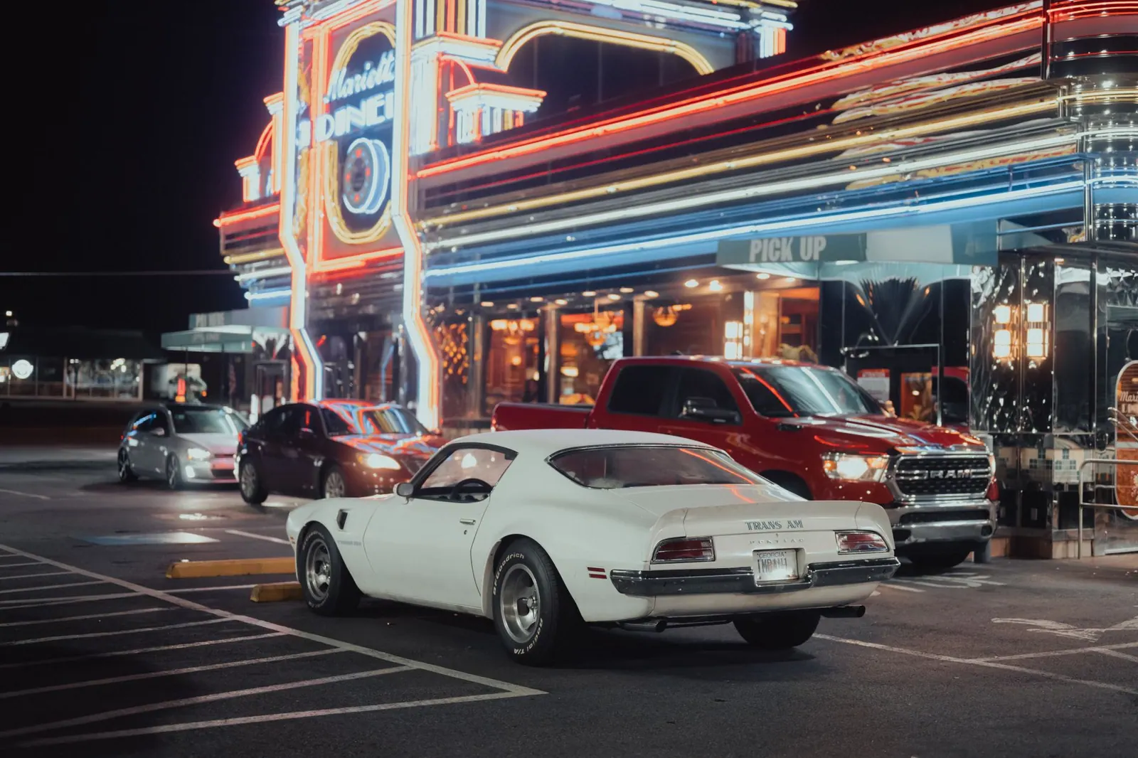 A vintage Pontiac Trans Am parked outside the vibrant Marietta Diner illuminated by neon lights at night.