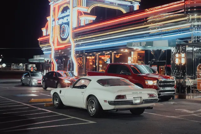 A vintage Pontiac Trans Am parked outside the vibrant Marietta Diner illuminated by neon lights at night.