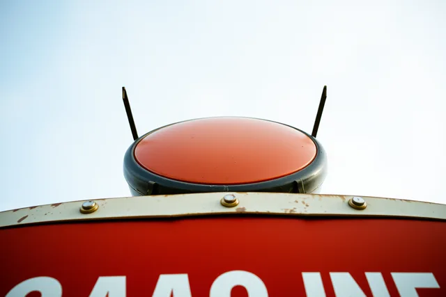 Porcelain-enamel gas station sign on rusted steel mounting brackets, enamel face chipped at bolt holes. Gas station preservation case study checklist: how to verify scope and sources before you publish