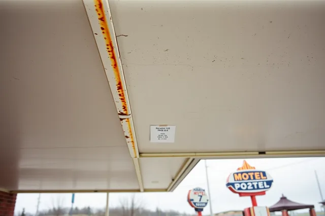 Rust-stained 1950s motel canopy soffit above neon sign and pump island. Historic motel restoration safety checklist: what owners must record in 2027
