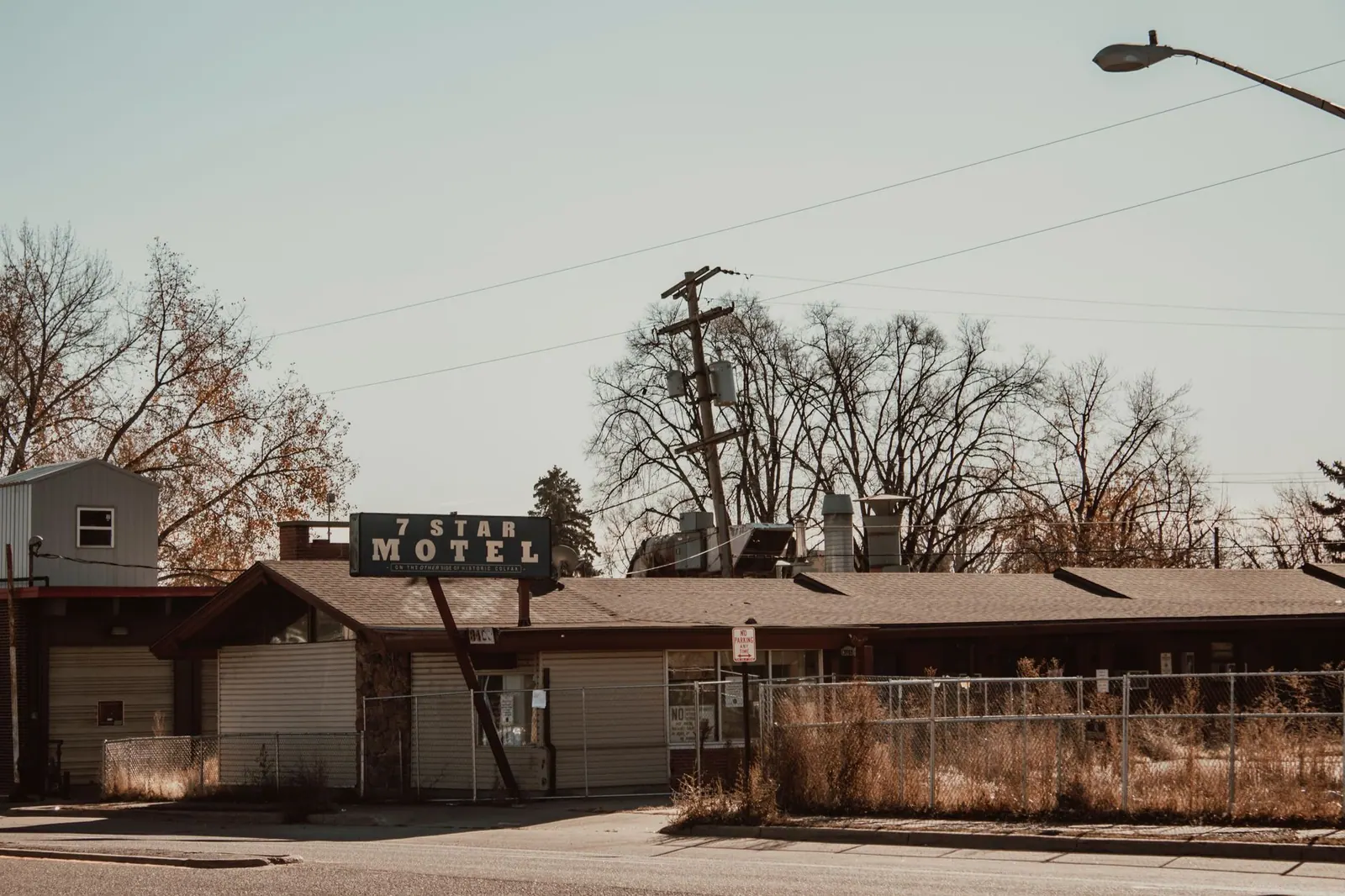 A vintage 7 Star Motel with a prominent sign, surrounded by tall grass and fencing, under a clear sky.