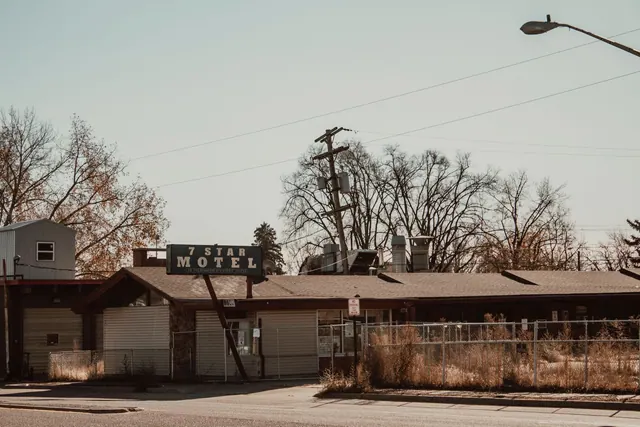 A vintage 7 Star Motel with a prominent sign, surrounded by tall grass and fencing, under a clear sky.