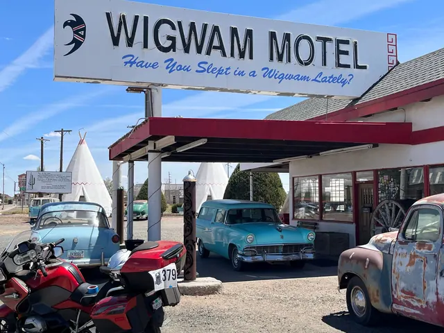 Vintage cars and Wigwam Motel sign in Holbrook, AZ, under a clear sky.