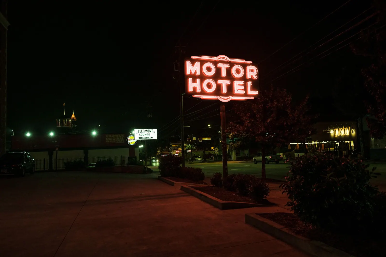 A glowing neon motor hotel sign illuminates the street at night, creating a retro ambiance.