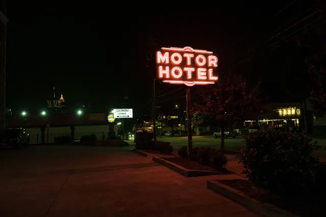 A glowing neon motor hotel sign illuminates the street at night, creating a retro ambiance.