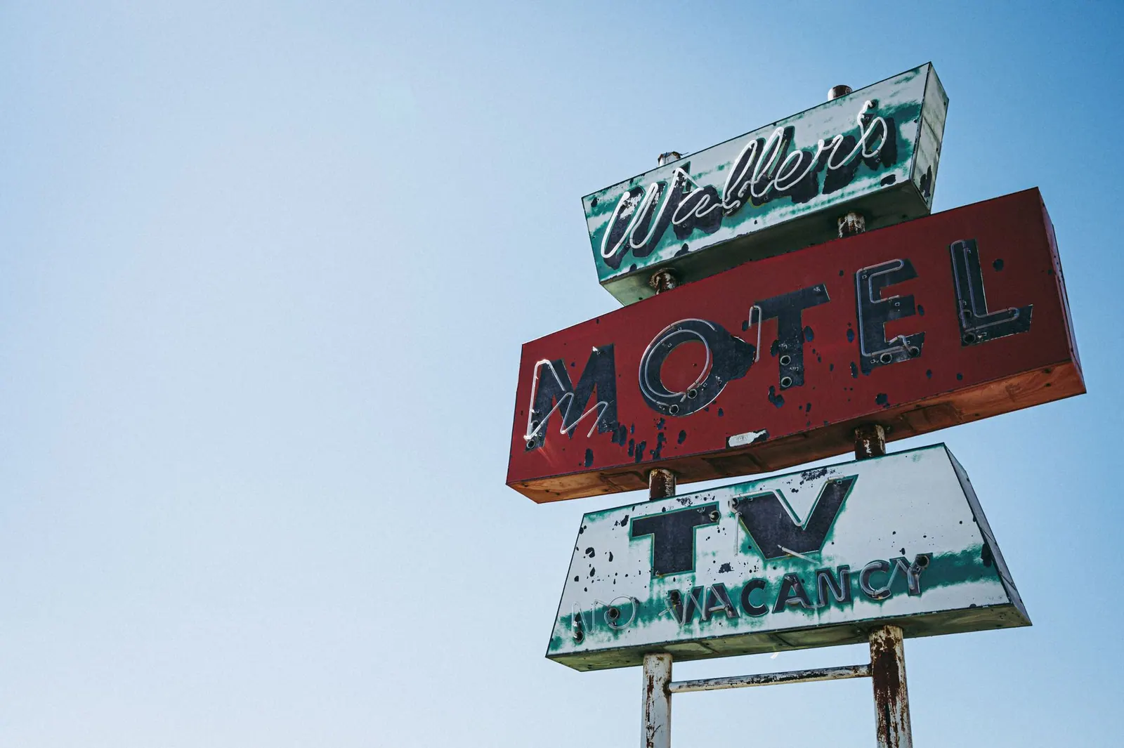 Old-fashioned motel sign featuring aged paint and retro neon lettering against a blue sky.