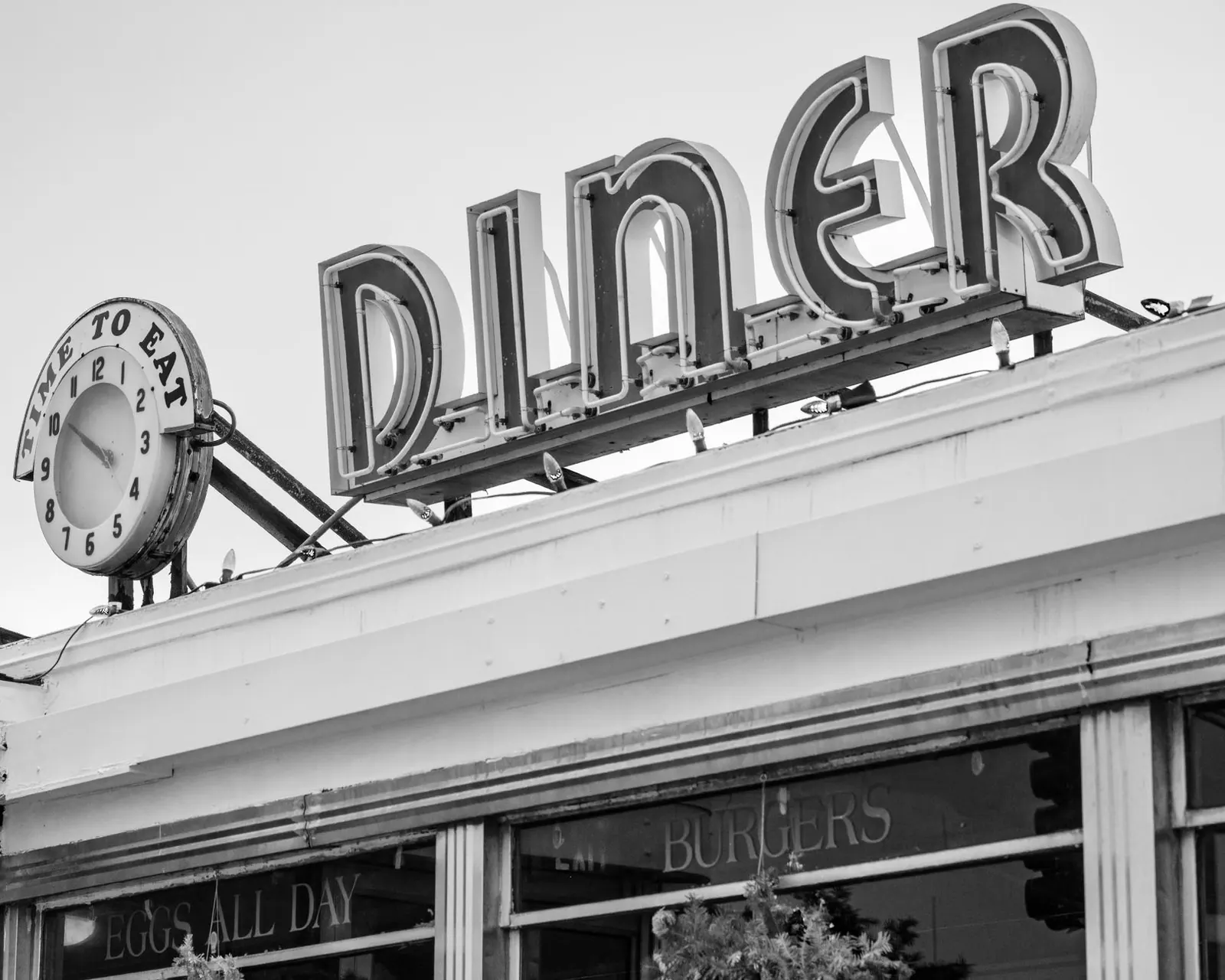 Black and white photo of a vintage diner sign with a clock in Somerville, MA.
