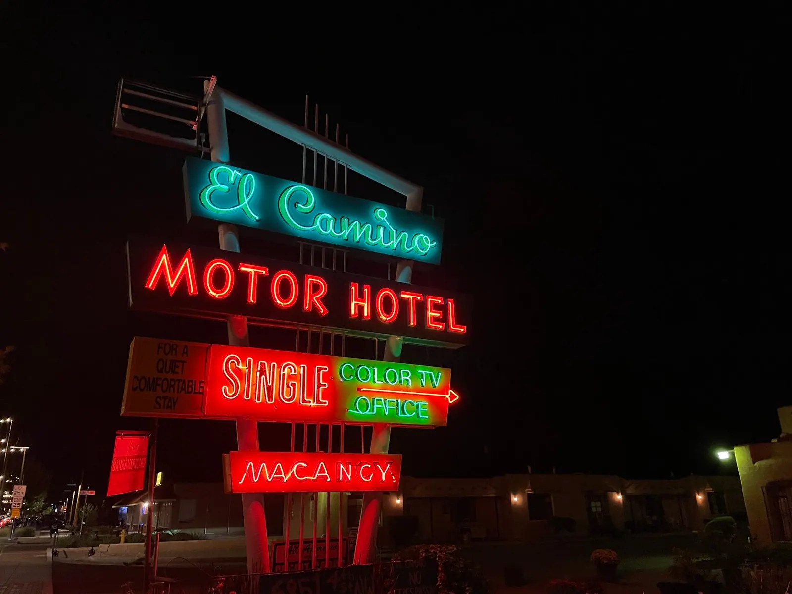 Colorful neon lights illuminate a vintage motel sign at night along the roadside.